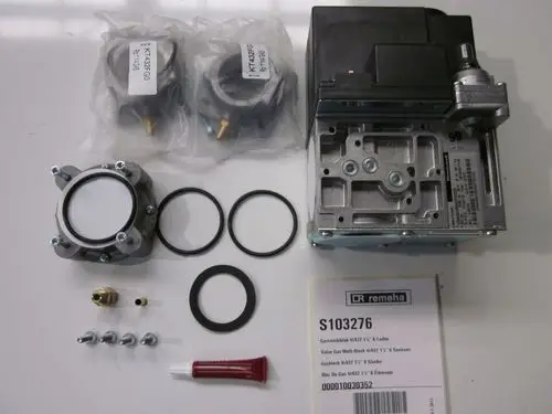 Remeha Gasblock mit Zubehörteilen im Vordergrund, darunter Dichtungen, Schrauben, und eine Tube Dichtmittel, auf hellem Untergrund angeordnet.